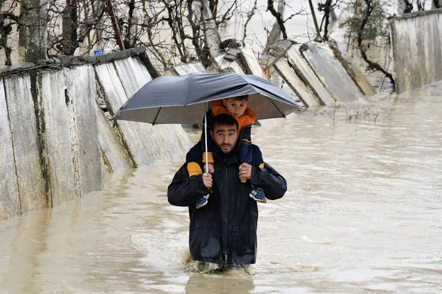 A man carries a child on his shoulders as he walks in a flooded street while leaving their houses in the village of Hasan, near Fushe Kruje, north of the capital Tirana, after heavy rainfalls, on December 1, 2017. .One person died and three others were injured after heavy rainfall over the past 36 hours that flooded many parts of Albania, paralyzing its ports and causing flights from its only international airport to be suspended. (Photo by Gent Shkullaku/AFP Photo)