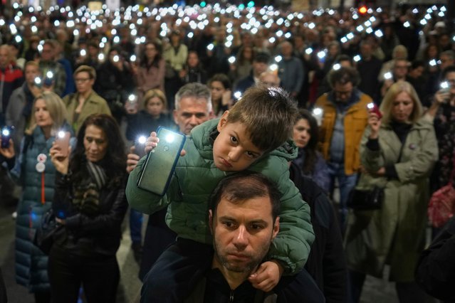 People stand in silence and hold up their mobile phone lights day after a 19-year-old has died, becoming the 16th fatality in the collapse of a railway concrete canopy fell in November, in Belgrade, Serbia, Saturday, March 22, 2025. (Photo by Darko Vojinovic/AP Photo)