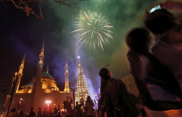 People watch fireworks go off near a giant Christmas tree, set in front of Muhammad al-Amin Mosque during Christmas celebrations at Martyr's Square in Beirut, Lebanon, Sunday, December 10, 2017. The fireworks mark the turning on of the Christmas tree lights.(Photo by Bilal Hussein/AP Photo)