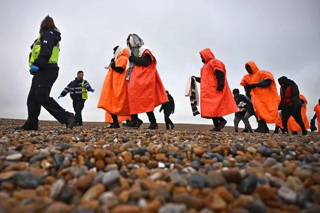 A British Immigration Enforcement officer (L) and an Interforce security officer (2L), escort migrants, picked up at sea by an Royal National Lifeboat Institution (RNLI) lifeboat whilst they were attempting to cross the English Channel, on the shore at Dungeness on the southeast coast of England, on December 9, 2022. (Photo by Ben Stansall/AFP Photo)