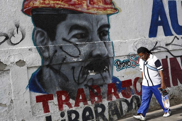 A man walks past a mural depicting Venezuela's President Nicolas Maduro in Caracas August 13, 2015. The mural reads, “Liberating work”. (Photo by Carlos Garcia Rawlins/Reuters)