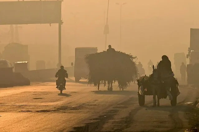 Commuters make their way along a street amid heavy smog in Lahore on November 18, 2022. (Photo by Arif Ali/AFP Photo)