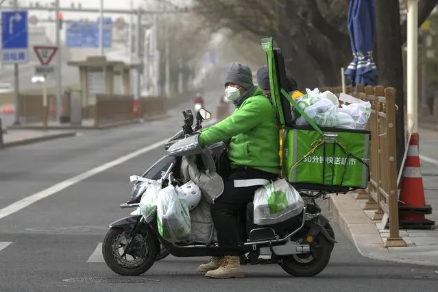 A delivery worker rides on his bike loaded with customers' online order groceries on a street in Beijing, Monday, December 12, 2022. China will drop a travel tracing requirement as part of an uncertain exit from its strict “zero-COVID” policies that have elicited widespread dissatisfaction. (Photo by Andy Wong/AP Photo)