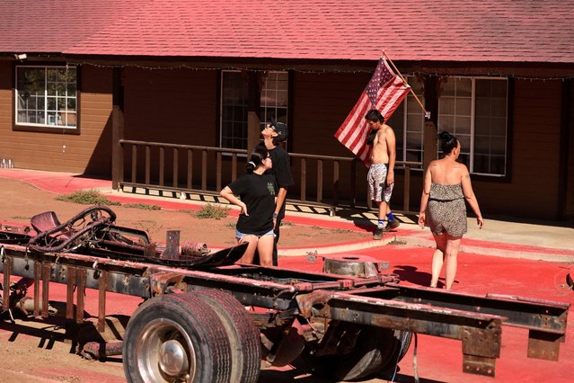 People walk in front of a house covered in fire retardant as firefighters tackle the Juniper Fire in Riverside County, California on July 1, 2025. (Photo by David Swanson/Reuters)