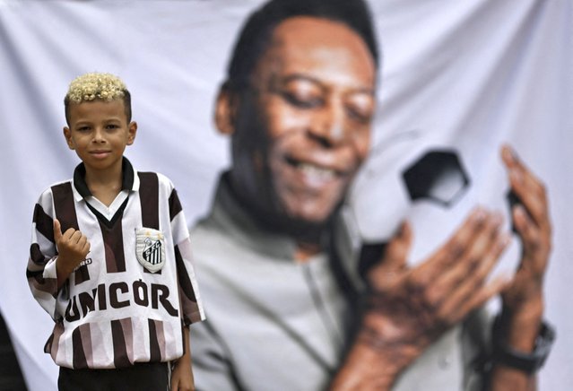 A young Santos fan poses in front of a banner of Brazilian soccer legend Pele, hung near his former club Santos' Vila Belmiro stadium, as his body lies in state on the pitch before the funeral in Santos, Brazil on January 2, 2023. (Photo by Ueslei Marcelino/Reuters)
