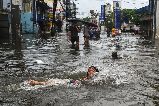 People wade through a flooded area in Malabon, metro Manila on July 24, 2025. The Philippines shut down schools and cancelled flights on July 24 as torrential rains driven by a typhoon and a separate tropical storm pounded the country's northern island of Luzon. (Photo by Jam Sta Rosa/AFP Photo)