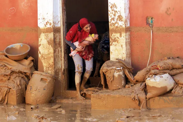 A picture taken October 29, 2016 shows a woman carrying her baby as she stands on her doorstep in Ras Gharib, near the mouth of the Gulf of Suez in the Red Sea governorate, after flooding in parts of Egypt caused by torrential rains. At least 22 people were killed and 72 injured in flooding in parts of Egypt caused by torrential rains, authorities said, updating an earlier toll of 18 dead. Ras Gharib, was the worst hit area with nine people killed in the flooding. (Photo by Mostafa El-Shemy/AFP Photo)