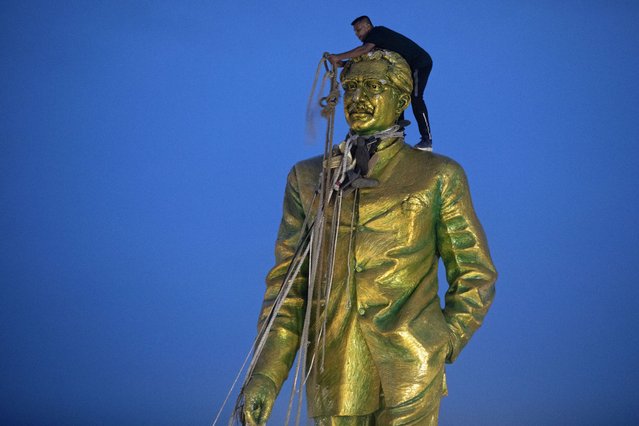 A man climbs to tie a rope around the head of a large statue of Sheikh Mujibur Rahman, father of Bangladesh leader Sheikh Hasina, as protesters try to bring it down after she resigned as Prime Minister, in Dhaka, Bangladesh, Monday, August 5, 2024. (Photo by Rajib Dhar/AP Photo)