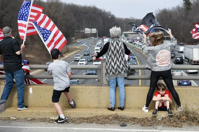 Jennifer Flebotte, right, stands along Georgetown Pike to watch a convoy make their way along Interstate 495 South as her son, Wilder tries to get out of the wind on Sunday March 06, 2022 in McLean, VA. The convoy, made up of truckers and other vehicles was protesting Covid-19 related mandates. They travelled from Hagerstown, MD Sunday and made two loops around the beltway. (Photo by Matt McClain/The Washington Post)