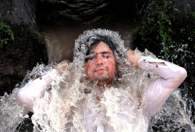 A man reacts as he cools off from the hot and sunny weather, under a water pipe from a canal on the outskirts of Peshawar, Pakistan May 29, 2018. (Photo by Fayaz  Aziz/Reuters)