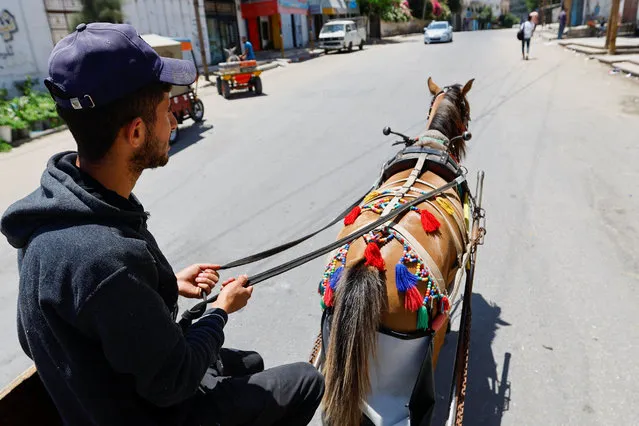 A Palestinian rides a cart drawn by a horse wearing a diaper, to keep the Gaza streets clean, in Deir Al-Balah, central Gaza Strip on June 5, 2023. (Photo by Ibraheem Abu Mustafa/Reuters)