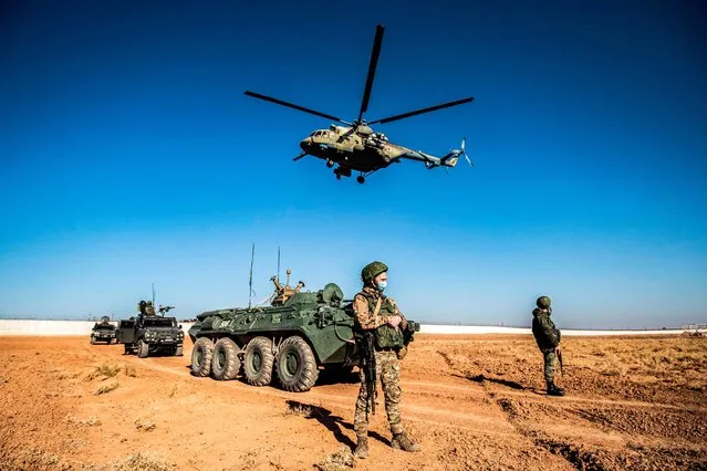 A Russian Mil Mi-17 military helicopter flies by soldiers and military vehicles during a joint Russian-Turkish patrol in the eastern countryside of the town of Darbasiyah near the border with Turkey in Syria's northeastern Hasakah province on December 7, 2020. (Photo by Delil Souleiman/AFP Photo)