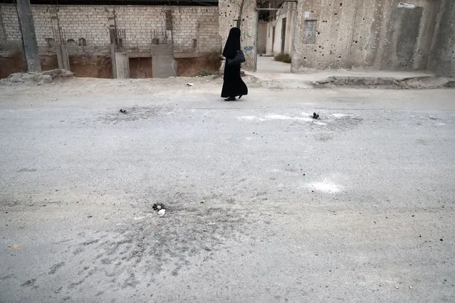 A fully- veiled woman walks past unexploded mortar shells in the rebel- held town of Douma on the eastern outskirts of the capital Damascus on November 13, 2016 Douma, the largest town in the Eastern Ghouta area with more than 100,000 residents, is surrounded and regularly shelled by regime forces. (Photo by Abd Doumany/AFP Photo)