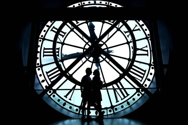 A couple poses for a photo near a giant clock at the Musee d'Orsay in Paris, on July 9, 2023. (Photo by Sergei Gapon/AFP Photo)