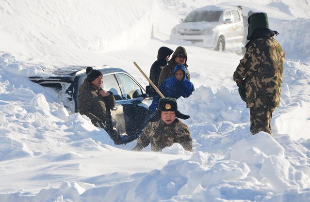 Police try to release a car trapped in a snow slide in Altay, Xinjiang Uighur Autonomous Region, January 3, 2016. (Photo by Reuters/China Daily)