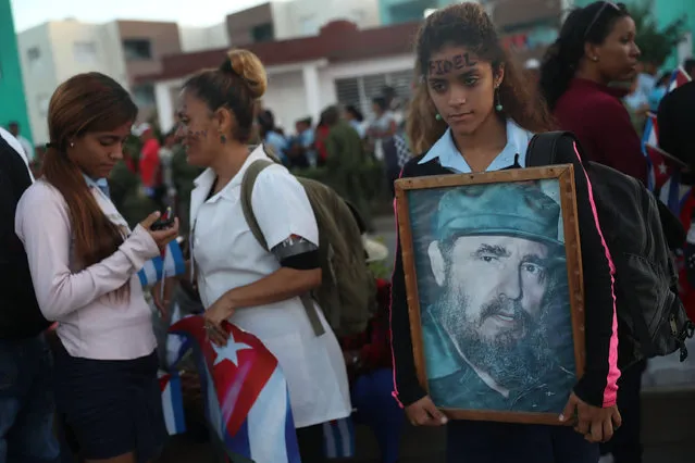 People hold a picture of former Cuban President Fidel Castro as they line a street to watch a military jeep towing a trailer with the flag draped chest containing his remains to drive past them to his burial at the Cementerio Santa Ifigenia on December 4, 2016 in Santiago de Cuba, Cuba. Mr. Castro died on November 25th at the age of 90. (Photo by Joe Raedle/Getty Images)