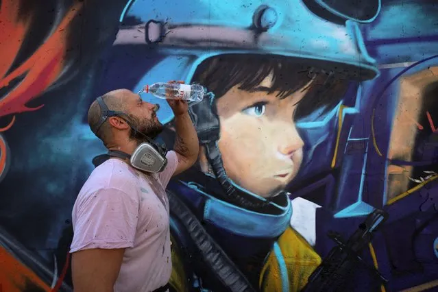 Davide Pianta, a graffiti artist from Italy, freshes himself with water in front of his mural as part of the Meeting of Styles graffiti festival in Kosovo's capital Pristina, Kosovo on July 29, 2023. (Photo by Fatos Bytyci/Reuters)