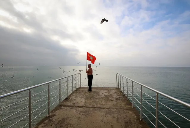 A man holds a Soviet flag as he stands on a pier during the opening of the cold water swimming season at the Back Sea town of Saky, Crimea November 24, 2018. (Photo by Pavel Rebrov/Reuters)