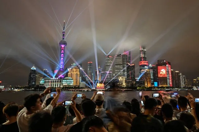 Spectators look at a light show on the Bund promenade in Shanghai on July 1, 2021, as the country marks the 100th anniversary of the founding of China's Communist Party. President Xi Jinping hailed China's “irreversible” course from colonial humiliation to great-power status at the centenary celebrations for the Chinese Communist Party, in a speech reaching deep into history to remind patriots at home and rivals abroad of his nation's – and his own – ascendancy. (Photo by Hector Retamal/AFP Photo)
