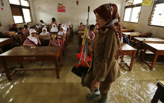 A teacher holding brooms and a dust pan walks in her flooded classroom in Lopang Domba Elementary School in Serang, Indonesia's Banten province November 13, 2013. The school has faced annual floods due to heavy rains during the monsoon season for more than seven years, according to school principal Munawaroh on Wednesday. (Photo by Reuters/Beawiharta)