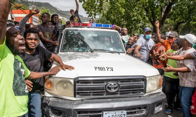People cheer as a police car drives past at the Petionville Police station where armed men, accused of being involved in the assassination of President Jovenel Moise, are being held in Port au Prince on July 8, 2021. Police in Haiti have surrounded a group of possible suspects in the assassination of President Jovenel Moise, the UN envoy to Haiti said. Helen La Lime said from the Haitian capital that four members of a group that attacked the presidential palace Wednesday and shot the president have been killed by police and six others are in custody. (Photo by Valerie Baeriswyl/AFP Photo)