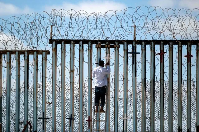 Josue Serrano, a Mexican deported migrant, hangs wooden crosses on the border fence as part of a vigil for migrants who died while migrating to the United States, at the US-Mexico border in playas de Tijuana, Baja California state, Mexico, on July 4, 2022. On June 27, 2022, 53 migrants from Mexico, Guatemala and Honduras were found death abandoned in a suffocatingly hot tractor-trailer truck in the US state of Texas. (Photo by Guillermo Arias/AFP Photo)