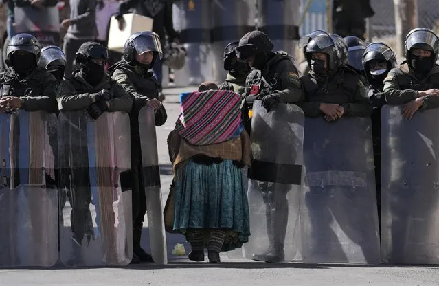 Police make way for an elderly woman to pass through while guarding the new coca leaf market during the third day of clashes in La Paz, Bolivia, Wednesday, August 3, 2022. Anti-government coca farmers are protesting against a parallel coca leaf market in La Paz. (Photo by Juan Karita/AP Photo)