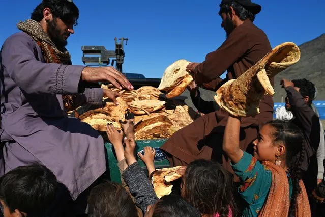 Afghan refugees' children receive bread from a local charity at a makeshift camp upon their arrival from Pakistan, near the Afghanistan-Pakistan Torkham border in Nangarhar province on November 12, 2023. More than 165,000 Afghans have fled Pakistan in the month since its government ordered 1.7 million people to leave or face arrest and deportation, officials said. (Photo by Wakil Kohsar/AFP Photo)