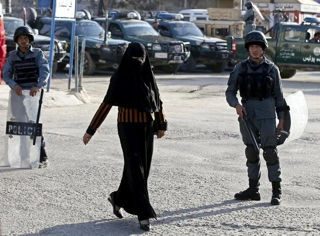 An Afghan woman walks while anti-raid policemen keep watch during a protest by Islamic clerics to condemn the killing of Farkhunda, a 27-year old woman, in Kabul March 26, 2015. The lynching of the woman by a mob in the Afghan capital continued to fuel public anger on Thursday, as residents gathered at the site of her death to protest a week after the killing. (Photo by Omar Sobhani/Reuters)