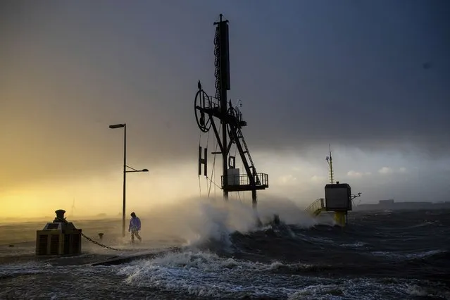 A person walks along the banks of the Weser estuary during a storm surge and waves in Bremerhaven, Germany, Friday December 22, 2023. Pre-Christmas rail travelers in parts of Germany faced widespread disruption on Friday as a storm swept across northern Europe, bringing down trees and prompting warnings of flooding on the North Sea coast. (Photo by Sina Schuldt/dpa via AP Photo)