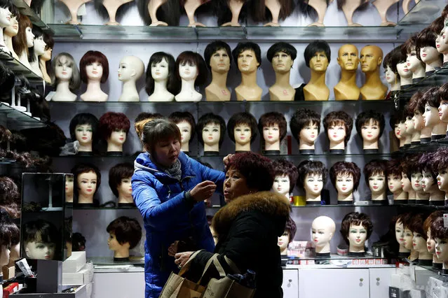 A vendor helps put on a wig on a customer at a wig shop near the central train station in Shanghai, China January 18, 2017. (Photo by Aly Song/Reuters)