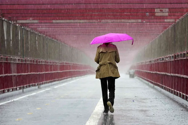 A pedestrian walks during a heavy downpour of rain over the Williamsburg bridge, Tuesday, October 26, 2021, in New York. A flash flood watch is in effect as a nor'easter moves through the New York metro area. (Photo by Mary Altaffer/AP Photo)
