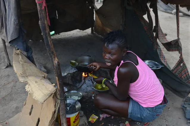 In this March 21, 2015 photo, a teenage girl is cooks the family's evening meal inside a makeshift tent of flattened cardboard boxes and cloth at a borderland encampment outside the southeast Haitian town of Anse-a-Pitres, Haiti. (Photo by David McFadden/AP Photo)