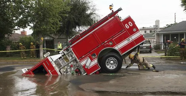 In this Tuesday, September 8, 2009 file photo, a Los Angeles firefighter looks under a fire truck stuck in a sinkhole in the Valley Village neighborhood of Los Angeles. Four firefighters escaped injury early Tuesday after their vehicle sunk into the hole caused by a burst water main in the San Fernando Valley, authorities said. (Photo by Nick Ut/AP Photo)
