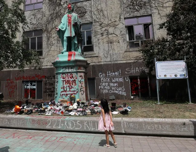 A girl looks up at the defaced Ryerson University statue of Egerton Ryerson, considered an architect of Canada's residential indigenous school system, following the discovery of the remains of 215 children on the site of British Columbia's former Kamloops Indian Residential School, in Toronto, Ontario, Canada on June 2, 2021. (Photo by Chris Helgren/Reuters)
