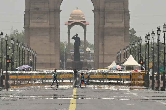 People walk past a mirage in front of the India Gate during a hot summer day in New Delhi on June 17, 2024. (Photo by Money Sharma/AFP Photo)