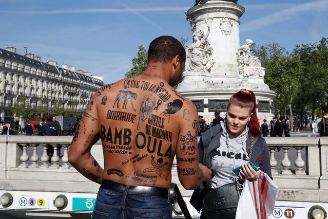 A man with his body covered with racist insults gives a flyer to a woman during an event organized by the Conseil Representatif des Associations Noires de France - CRAN (Representative Council of France' s Black Associations) to protest against racism, on the place de la Republique in Paris on April 24, 2017, one day after moderate candidate Emmanuel Macron won the first round of France' s presidential election and looked set to triumph in the run- off against far- right candidate Marine Le Pen next month. (Photo by Francois Guillot/AFP Photo)