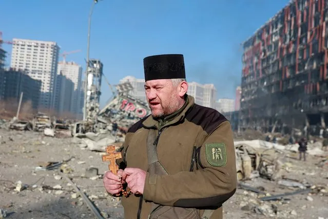 Chaplain Mykola Medinsky holds a cross and a rosary at the site of a military strike on a shopping center in the Podilskyi district of Kyiv, as Russia's invasion of Ukraine continues, in Kyiv, Ukraine on March 21, 2022. (Photo by Serhii Nuzhnenko/Reuters)