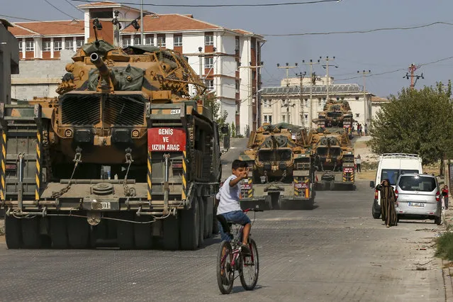 Children watch as army tanks are transported on trucks in the outskirts of the town of Akcakale, in Sanliurfa province, southeastern Turkey, at he border of Syria, Thursday, October 17, 2019. U.S. Vice President Mike Pence, heading a delegation that includes Secretary of State Mike Pompeo and White House national security adviser Robert O'Brien, arrived in Turkey on Thursday, a day after Trump dismissed the very crisis he sent his aides on an emergency mission to douse. (Photo by Emrah Gurel/AP Photo)