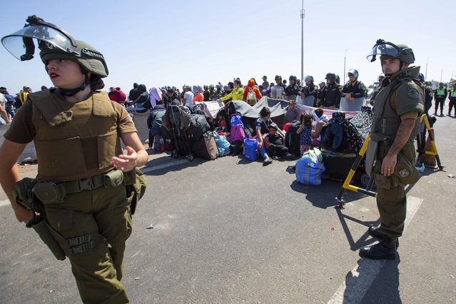 Carabineros stand close to migrants sitting on the road near Arica, Chile, Thursday, April 27, 2023. A migration crisis at the border between Chile and Peru is intensifying, with hundreds of people stranded, unable to cross into Peru in an effort to return to their homes. (Photo by Patricio Banda/Aton Chile via AP Photo)