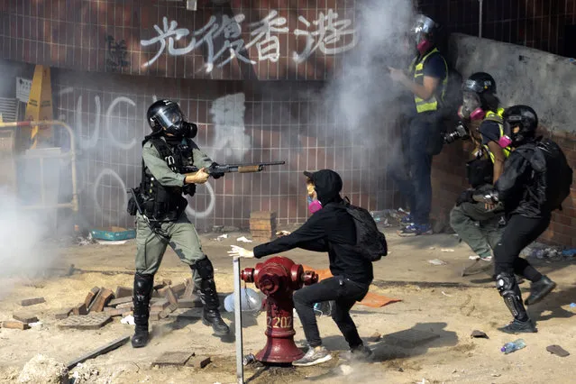 A policeman in riot gear points his weapon as protesters try to flee from the Hong Kong Polytechnic University in Hong Kong, Monday, November 18, 2019. Hong Kong police have swooped in with tear gas and batons as protesters who have taken over the university campus make an apparent last-ditch effort to escape arrest. (Photo by Ng Han Guan/AP Photo)
