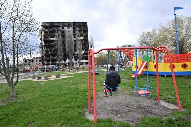 A teenager sits on a swing in a play ground opposit an apartment block destroyed in bombardment, in the Ukrainian town of Borodianka, in the Kyiv region on April 17, 2022. Russia invaded Ukraine on February 24, 2022. (Photo by Sergei Supinsky/AFP Photo)