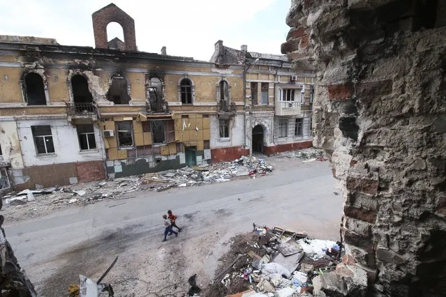 Children walk among buildings destroyed during fighting in Mariupol, in territory under the government of the Donetsk People's Republic, eastern Ukraine, Wednesday, May 25, 2022. (Photo by AP Photo/Stringer)