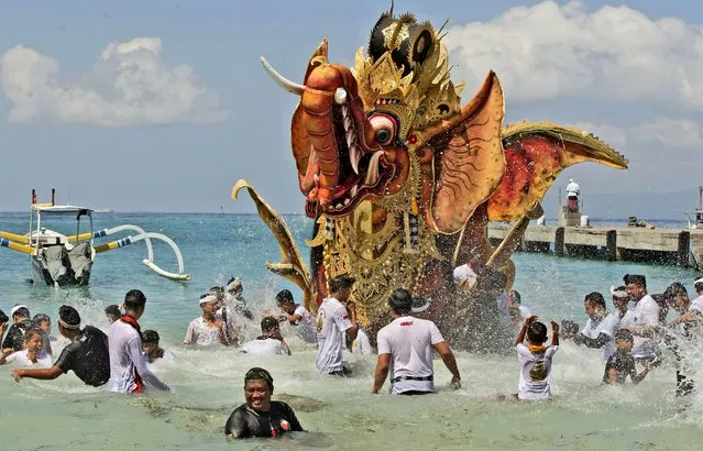 Balinese men parade a giant effigy of a mythical animal which later will be burned during a traditional mass cremation ceremony called “ngaben” on a beach on Friday, July 29, 2022, in Padangbai, Bali, Indonesia. Balinese believe that cremating the dead liberates their souls, allowing them to enter the higher world to reincarnate into better beings. (Photo by Firdia Lisnawati/AP Photo)