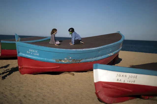 Two children wearing face masks sit on top of a boat in a beach in Badalona, near Barcelona, Spain, Tuesday, April 28, 2020 as the lockdown to combat the spread of coronavirus continues. Health authorities in Spain are urging parents to be responsible and abide by social distancing rules a day after some beach fronts and city promenades filled with families eager to enjoy the first stroll out in six weeks. (Photo by Emilio Morenatti/AP Photo)