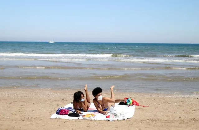 Women wearing face masks sunbathe at the Malvarrosa beach, as some Spanish provinces are allowed to ease lockdown restrictions during phase one, in Valencia, Spain, May 18, 2020. (Photo by Nacho Doce/Reuters)