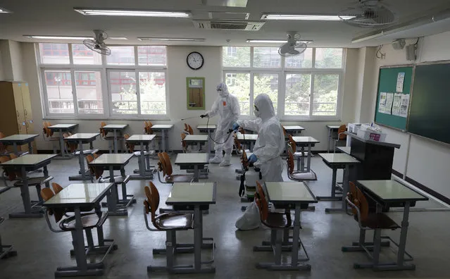 Health officials wearing protective gear spray disinfectant to help reduce the spread the new coronavirus ahead of school reopening in a cafeteria at a high school in Seoul, South Korea, Monday, May 11, 2020. (Photo by Lee Jin-man/AP Photo)