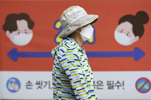A woman wearing a face mask to help protect against the spread of the new coronavirus passes by a banner about precautions against the virus at a park in Goyang, South Korea, Tuesday, June 2, 2020. Areas around the South Korean capital moved to curb large gatherings Tuesday and officials urged churchgoers and some health care workers to avoid crowds as the number of new coronavirus once again increased. (Photo by Ahn Young-joon/AP Photo)