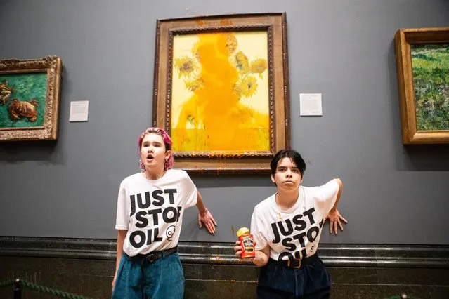A handout picture from the Just Stop Oil climate campaign group shows activists with their hands glued to the wall under Vincent van Gogh's “Sunflowers” after throwing tomato soup on the painting at the National Gallery in central London on October 14, 2022. London's Metropolitan Police said its officers arrested two protesters from the Just Stop Oil group for criminal damage and aggravated trespass after they “threw a substance over a painting” at the gallery on Trafalgar Square. (Photo by Antonio Olmos/The Guardian)