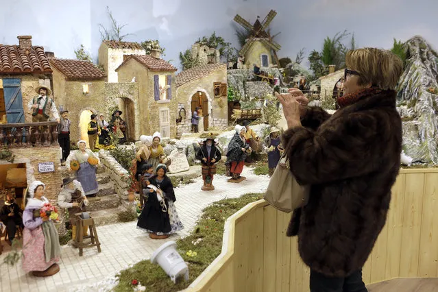 A woman photographs a crib in the village of Aubagne, near Marseille, southern France, Thursday, November 30, 2017. Craftsmen of the city joined their forces to build a traditional provencal crib that shows 3 500 clay made figurines named santons. Santons are traditional colored figurines usually set in Christmas Nativity scenes. (Photo by Claude Paris/AP Photo)